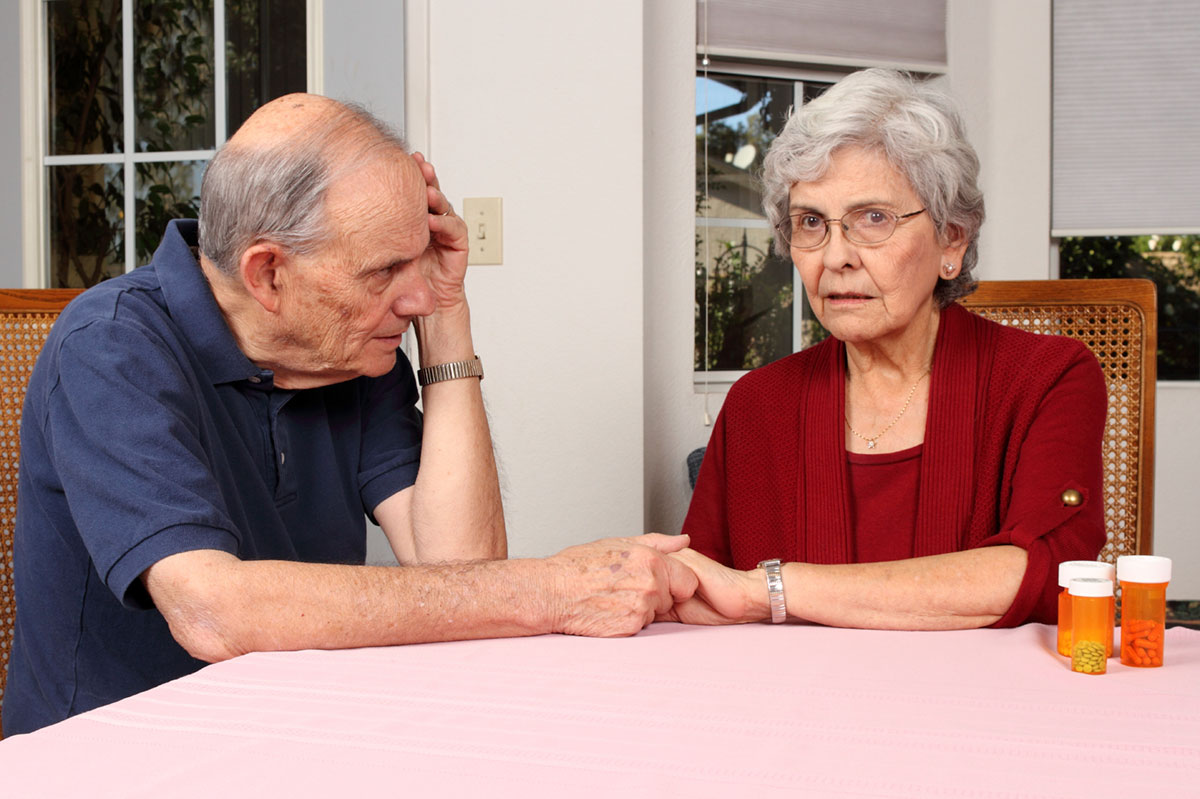 concerned elderly couple sitting at a table and holding hands